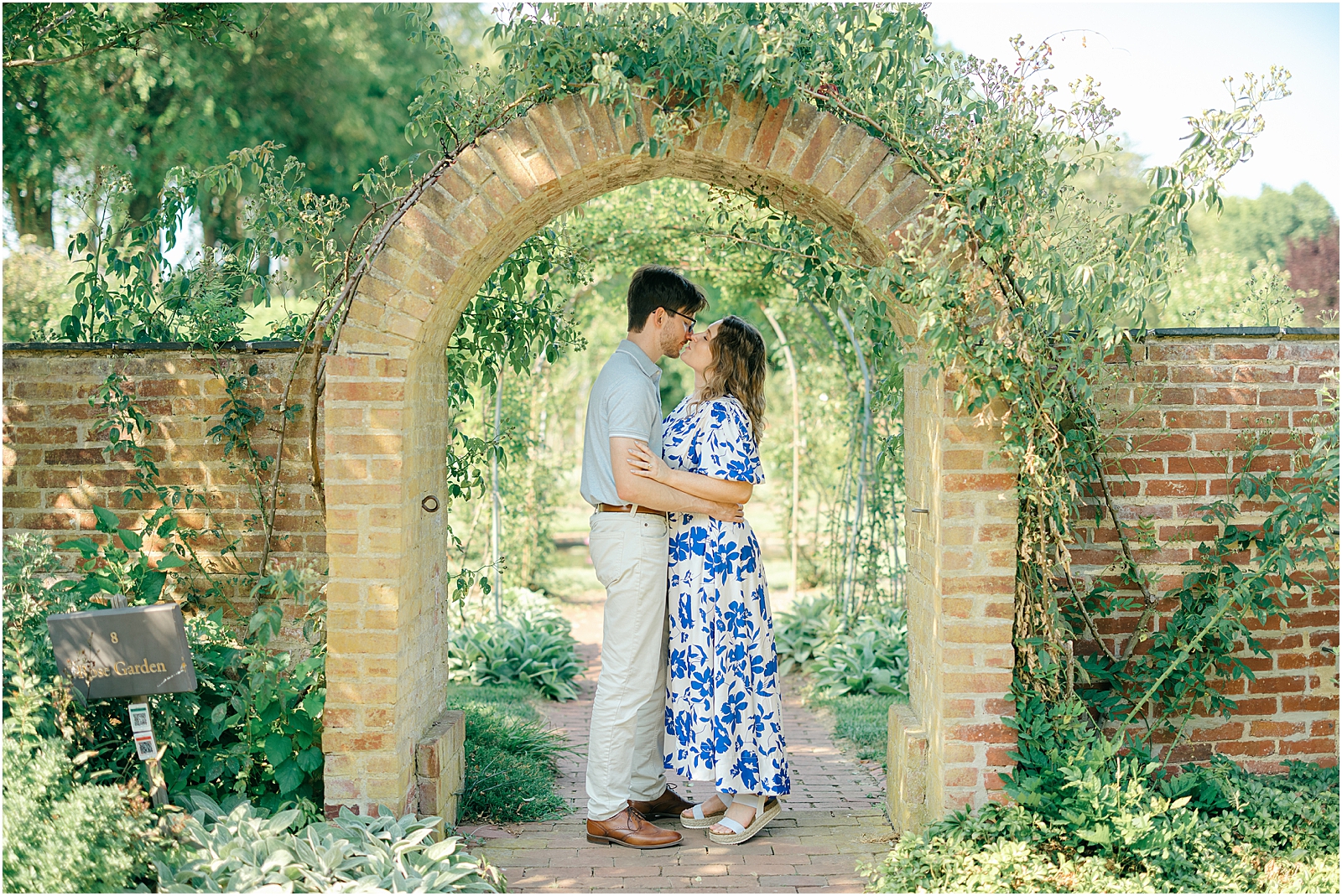 Engaged couple kissing beneath the brick archway at Ladew Topiary Gardens during their Maryland engagement session.
