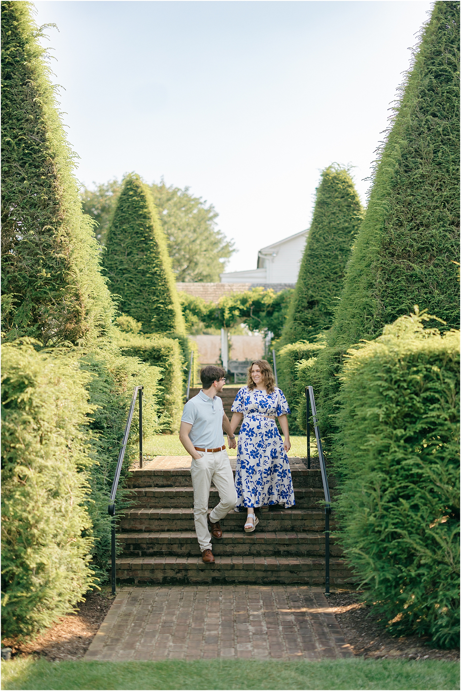 Engaged couple walking down brick steps surrounded by tall topiary hedges at Ladew Topiary Gardens.