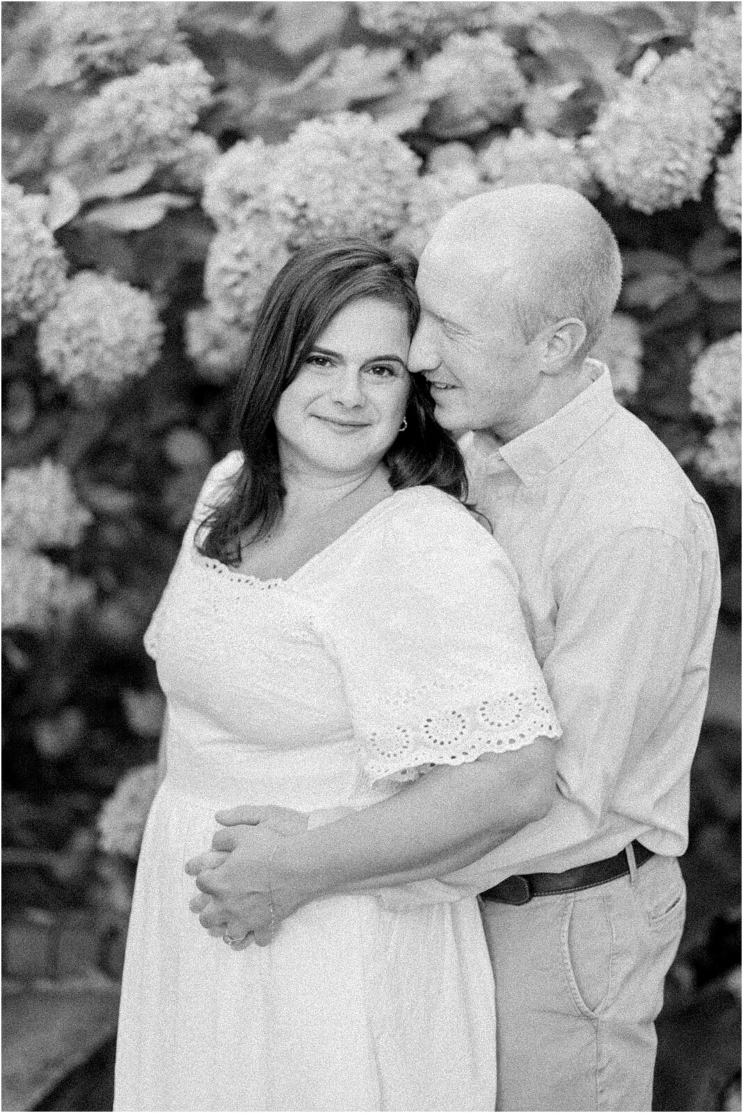 black and white photo of couple posing in front of hydrangeas in downtown middleburg for engagement photos.